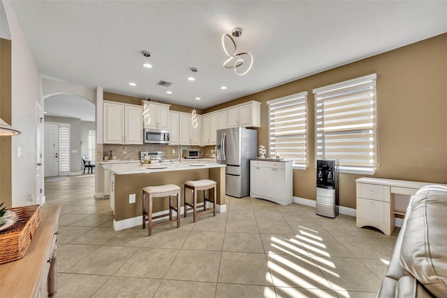 kitchen with a center island, decorative backsplash, light tile patterned floors, appliances with stainless steel finishes, and decorative light fixtures