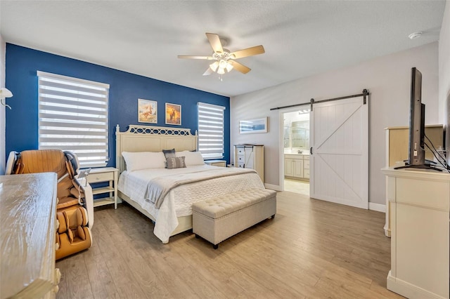 bedroom with ceiling fan, a barn door, light hardwood / wood-style floors, and connected bathroom