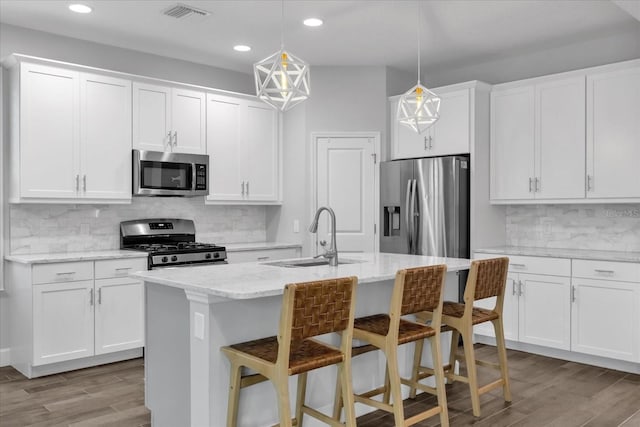 kitchen featuring stainless steel appliances, sink, pendant lighting, a center island with sink, and white cabinets