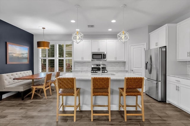 kitchen featuring light stone countertops, hanging light fixtures, decorative backsplash, a kitchen island with sink, and appliances with stainless steel finishes