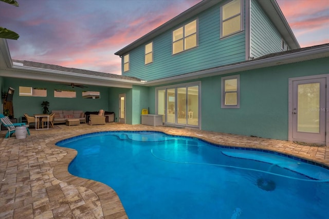 pool at dusk featuring outdoor lounge area, ceiling fan, and a patio