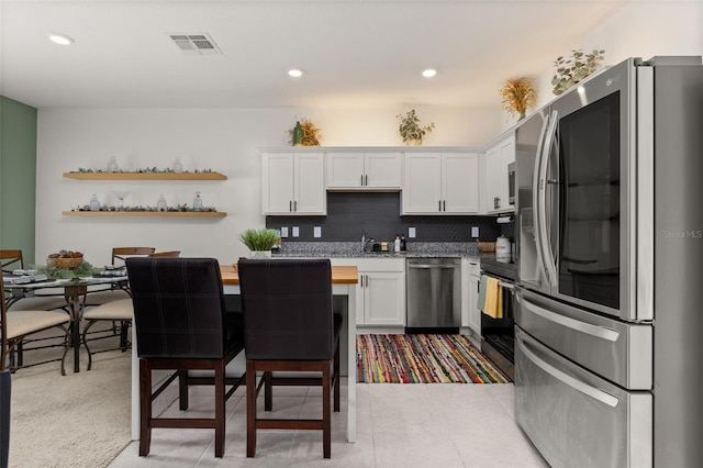 kitchen featuring decorative backsplash, stainless steel appliances, sink, light tile patterned floors, and white cabinets