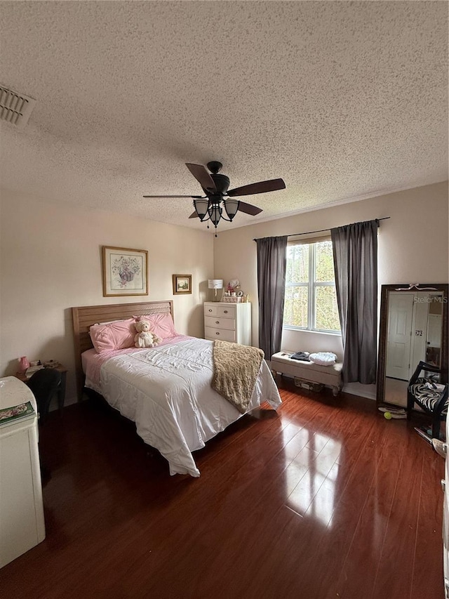 bedroom with a textured ceiling, ceiling fan, and dark wood-type flooring