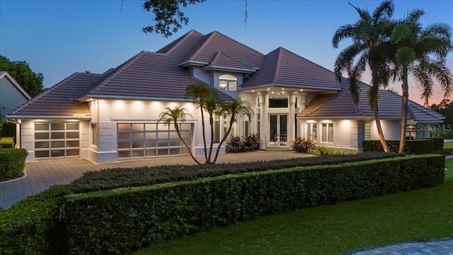 back house at dusk featuring french doors and a garage