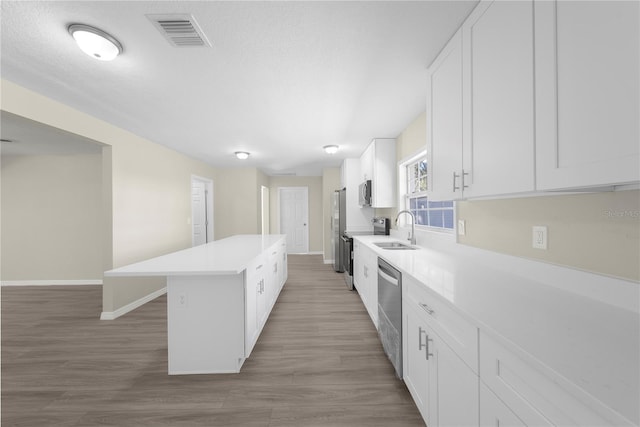 kitchen with hardwood / wood-style floors, a kitchen island, sink, white cabinetry, and appliances with stainless steel finishes