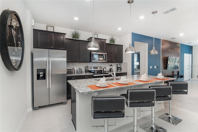 kitchen with pendant lighting, a center island with sink, light stone countertops, and stainless steel appliances