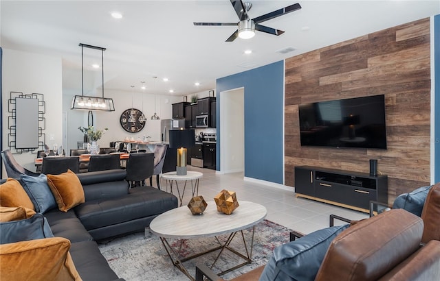 living room featuring ceiling fan, wood walls, and light tile patterned floors