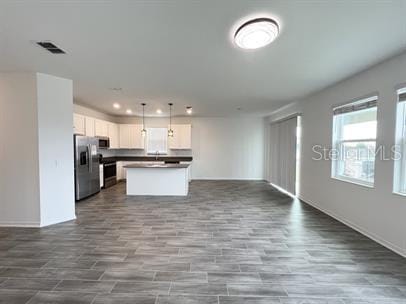 kitchen featuring white cabinetry, range, a center island, hanging light fixtures, and stainless steel fridge