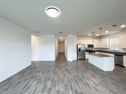 kitchen featuring dark wood-type flooring, appliances with stainless steel finishes, white cabinetry, hanging light fixtures, and a kitchen island