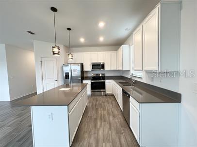 kitchen featuring pendant lighting, sink, white cabinetry, stainless steel appliances, and a kitchen island