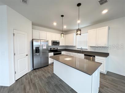 kitchen with appliances with stainless steel finishes, a kitchen island, white cabinetry, sink, and hanging light fixtures