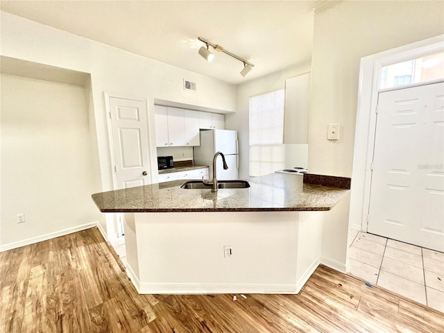 kitchen featuring rail lighting, kitchen peninsula, sink, white fridge, and white cabinetry