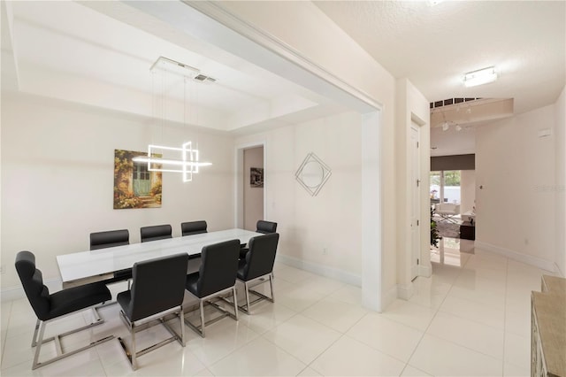 dining space with a textured ceiling, a raised ceiling, and light tile patterned flooring