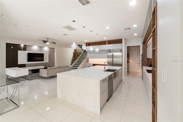 kitchen with ceiling fan, light tile patterned floors, appliances with stainless steel finishes, a large island, and light stone counters