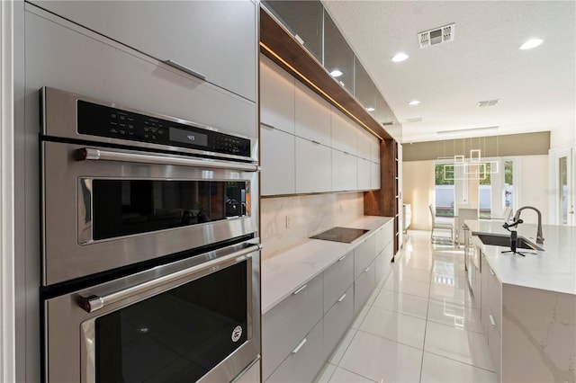 kitchen featuring light stone counters, stainless steel double oven, a textured ceiling, sink, and light tile patterned floors