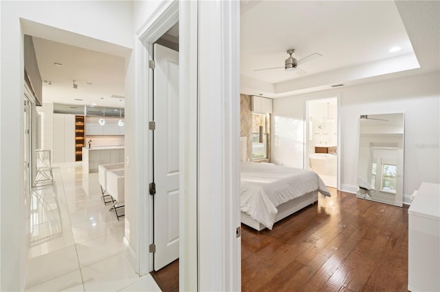 bedroom with ceiling fan, a raised ceiling, wood-type flooring, and connected bathroom