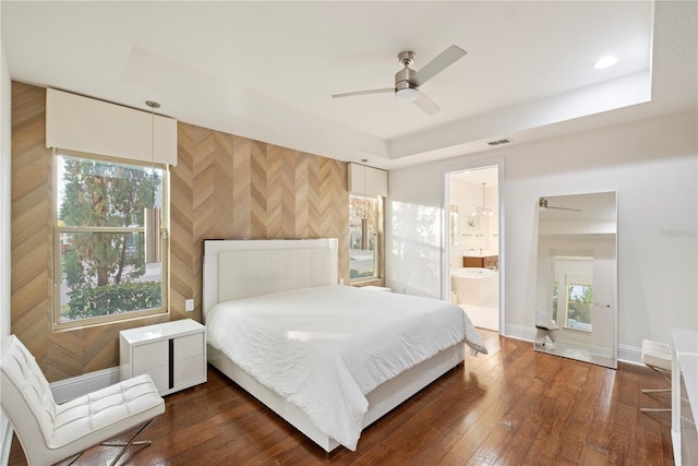 bedroom with a raised ceiling, connected bathroom, ceiling fan, and dark hardwood / wood-style floors