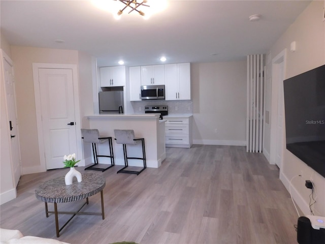 kitchen with backsplash, white cabinets, light wood-type flooring, appliances with stainless steel finishes, and a breakfast bar area