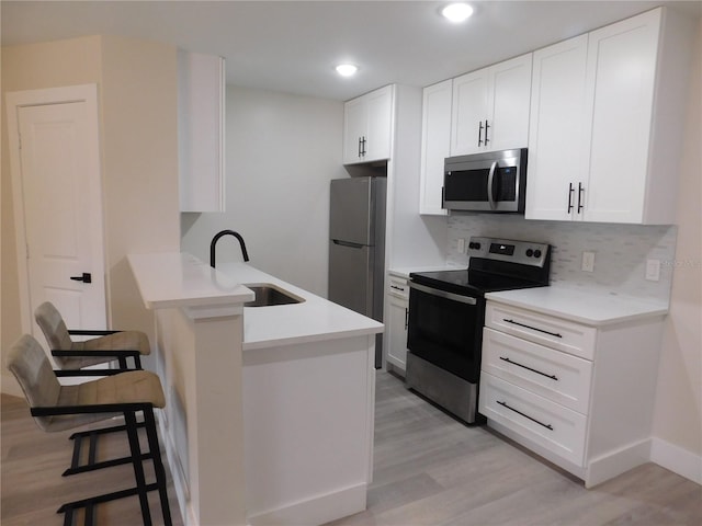 kitchen with a kitchen bar, appliances with stainless steel finishes, sink, light hardwood / wood-style floors, and white cabinetry