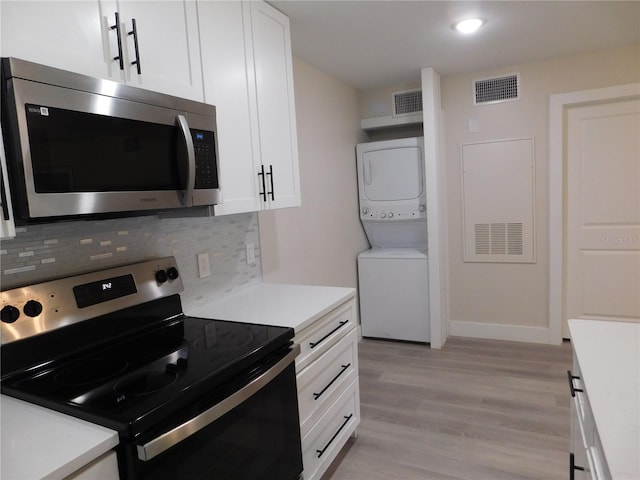 kitchen featuring backsplash, light wood-type flooring, appliances with stainless steel finishes, stacked washer / drying machine, and white cabinetry