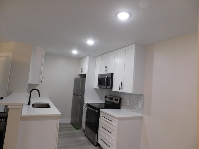 kitchen with kitchen peninsula, appliances with stainless steel finishes, backsplash, sink, and white cabinetry