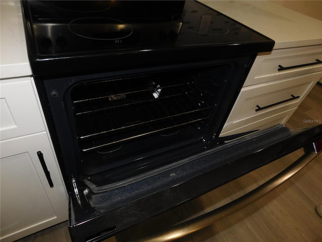 room details with white cabinets, black stove, and dark hardwood / wood-style flooring