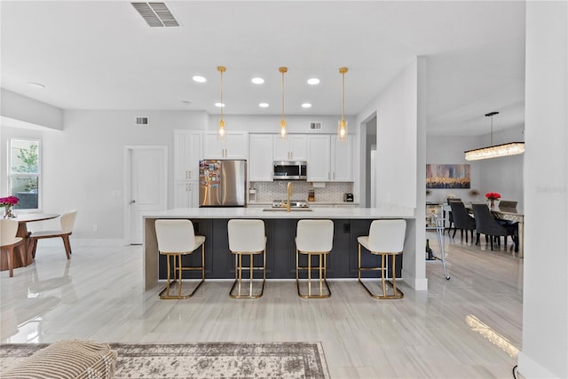 kitchen with decorative backsplash, white cabinetry, stainless steel appliances, and hanging light fixtures