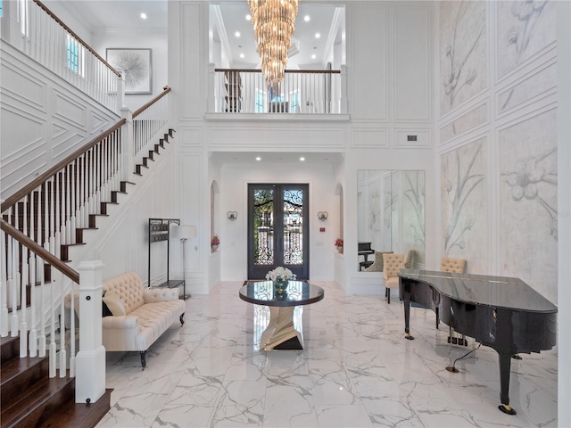 entryway with a notable chandelier, a towering ceiling, crown molding, and french doors