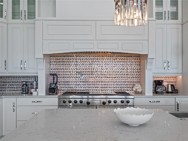 kitchen featuring range, hanging light fixtures, light stone countertops, tasteful backsplash, and white cabinetry