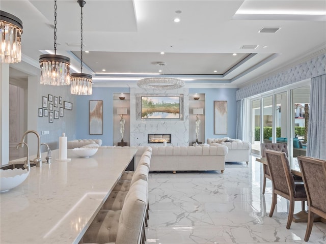 interior space featuring pendant lighting, a raised ceiling, sink, light stone countertops, and ornamental molding