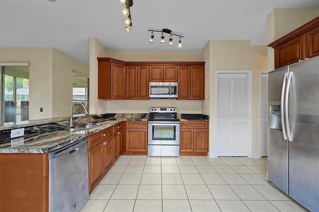 kitchen featuring appliances with stainless steel finishes, light tile patterned floors, dark stone counters, and sink