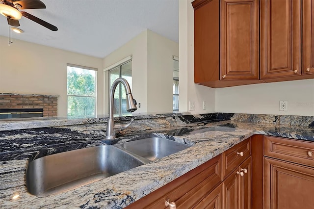 kitchen with a fireplace, light stone counters, sink, and ceiling fan