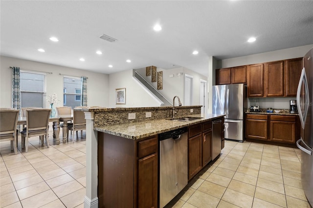 kitchen with sink, light tile patterned floors, stainless steel appliances, and a kitchen island with sink