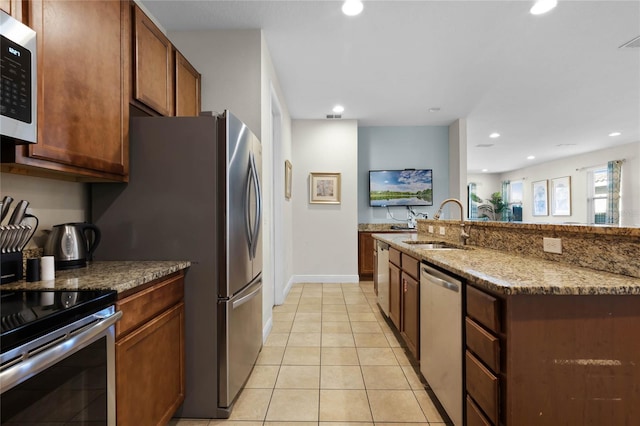 kitchen featuring a center island with sink, sink, light stone countertops, light tile patterned floors, and stainless steel appliances