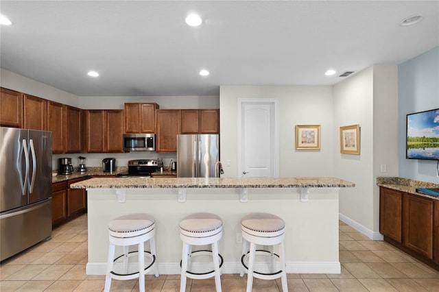 kitchen featuring a breakfast bar, appliances with stainless steel finishes, a kitchen island, and light stone countertops