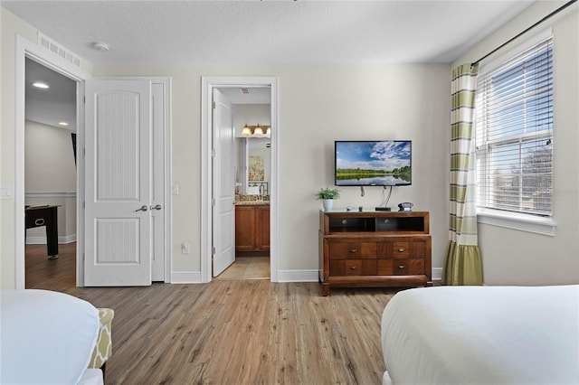 bedroom with connected bathroom, light hardwood / wood-style flooring, and multiple windows