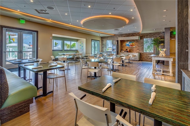 dining room with light hardwood / wood-style floors, a drop ceiling, and brick wall