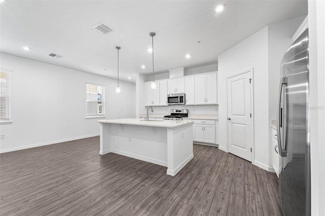 kitchen with hanging light fixtures, appliances with stainless steel finishes, a kitchen island with sink, and white cabinets