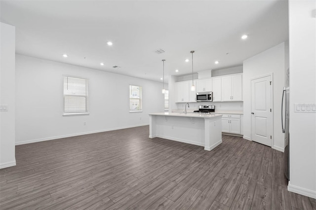 kitchen featuring pendant lighting, appliances with stainless steel finishes, white cabinetry, an island with sink, and dark hardwood / wood-style flooring