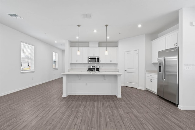 kitchen with stainless steel appliances, white cabinetry, wood-type flooring, and decorative light fixtures