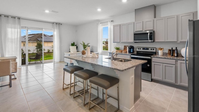 kitchen featuring appliances with stainless steel finishes, light stone counters, a breakfast bar, a kitchen island with sink, and sink