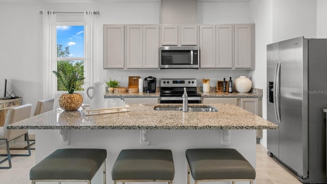 kitchen featuring light stone counters, a breakfast bar area, a kitchen island with sink, light tile patterned flooring, and appliances with stainless steel finishes