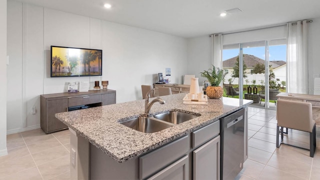 kitchen featuring a center island with sink, sink, stainless steel dishwasher, light tile patterned flooring, and light stone counters