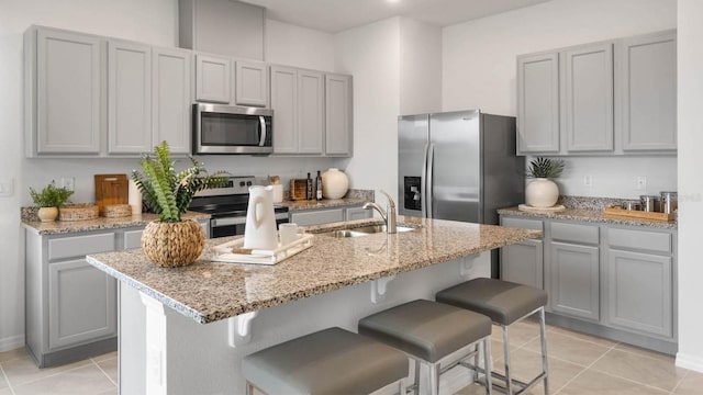 kitchen featuring light tile patterned flooring, stainless steel appliances, a center island with sink, and sink