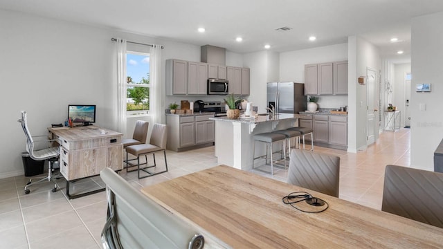 interior space featuring a breakfast bar area, gray cabinets, a center island with sink, and appliances with stainless steel finishes