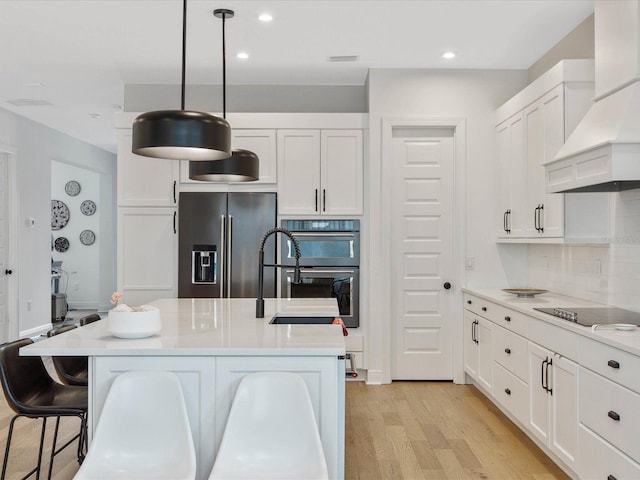 kitchen with pendant lighting, white cabinetry, stainless steel appliances, and a kitchen island with sink