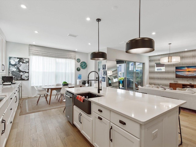 kitchen with white cabinetry, sink, hanging light fixtures, light hardwood / wood-style flooring, and an island with sink