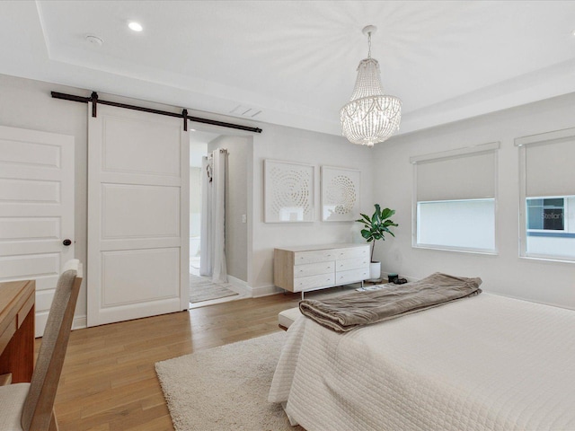 bedroom with light wood-type flooring, a barn door, a raised ceiling, and a notable chandelier