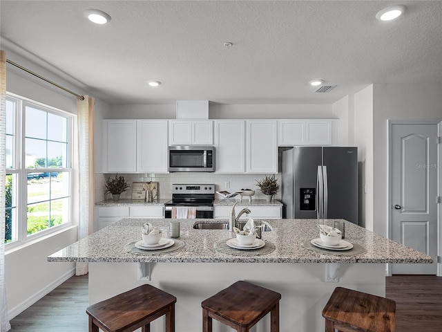 kitchen featuring white cabinets, appliances with stainless steel finishes, a breakfast bar, and a kitchen island with sink