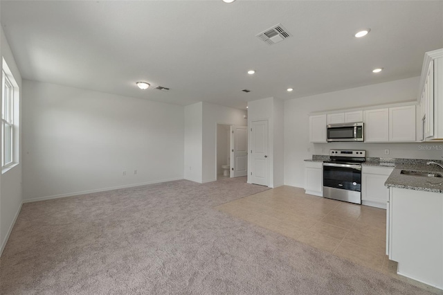 kitchen with light stone counters, white cabinets, stainless steel appliances, and light colored carpet